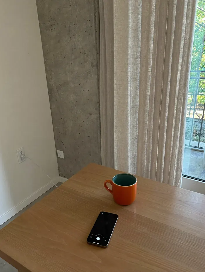 Pomarańczowy kubek i telefon na dębowym stole w jasnym mieszkaniu